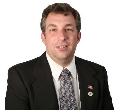 headshot of a person in black blazer, white button up shirt, and patterned tie in front of a white backdrop headshot of a person in black blazer, white button up shirt, and patterned tie in front of a white backdrop